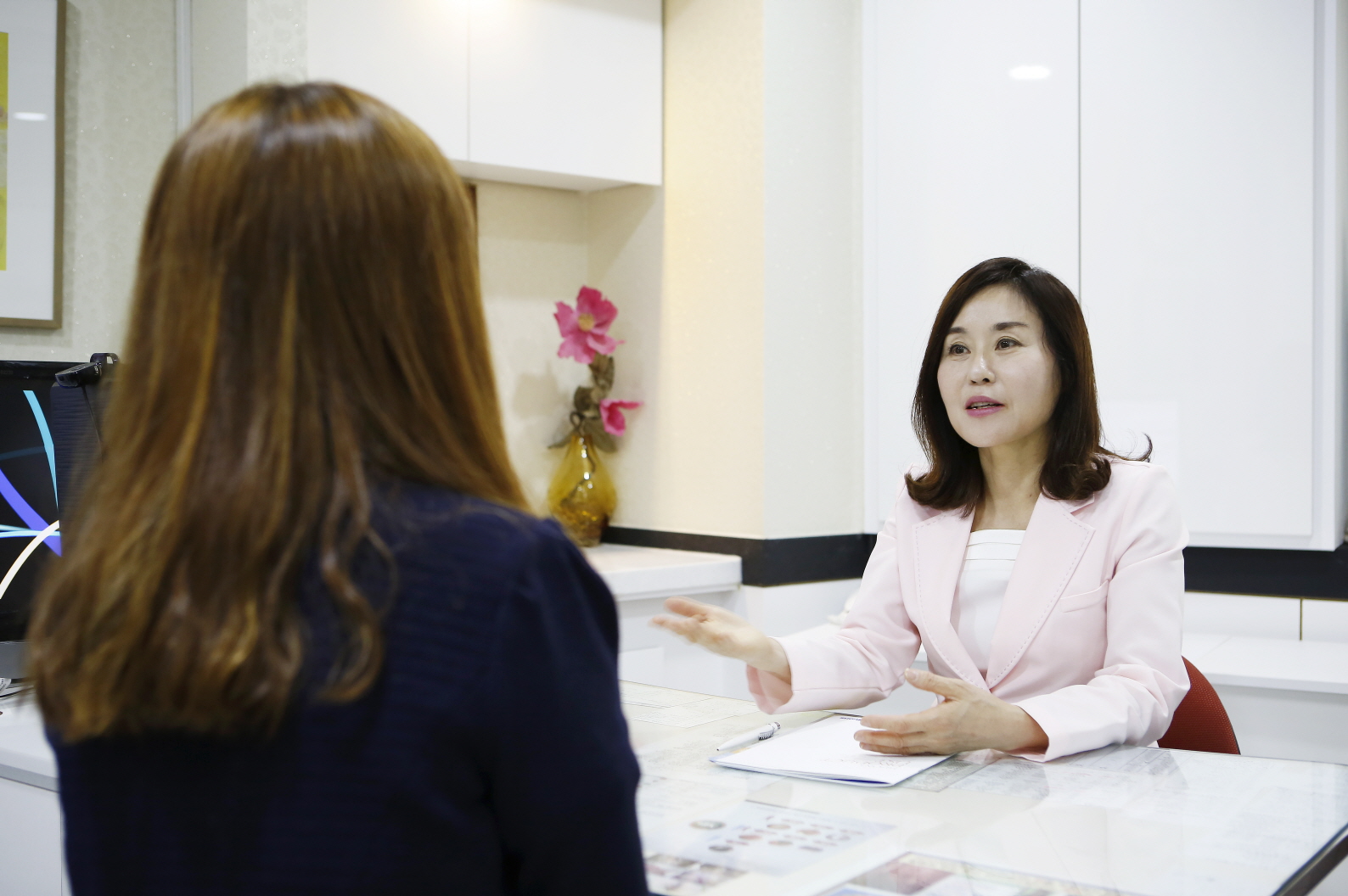 분홍 재킷을 입은 중년 여성이 상담 테이블 맞은편에 앉은 환자와 대화하는 상담실 사진