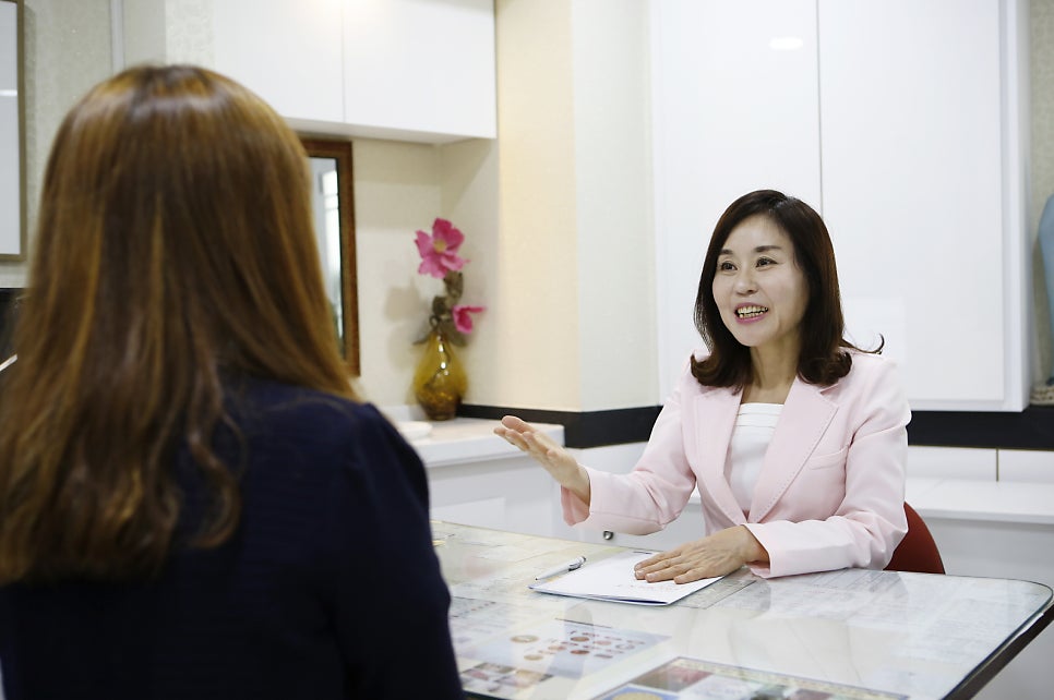 핑크색 재킷을 입은 원장이 환자와 진료실 책상에서 상담하며 손짓하는 사진